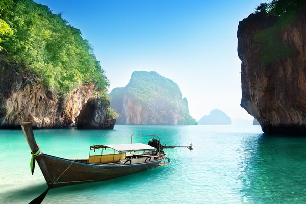 Una barca a coda lunga ormeggiata in una baia verde chiusa fra due pareti di roccia calcarea, in provincia di Krabi